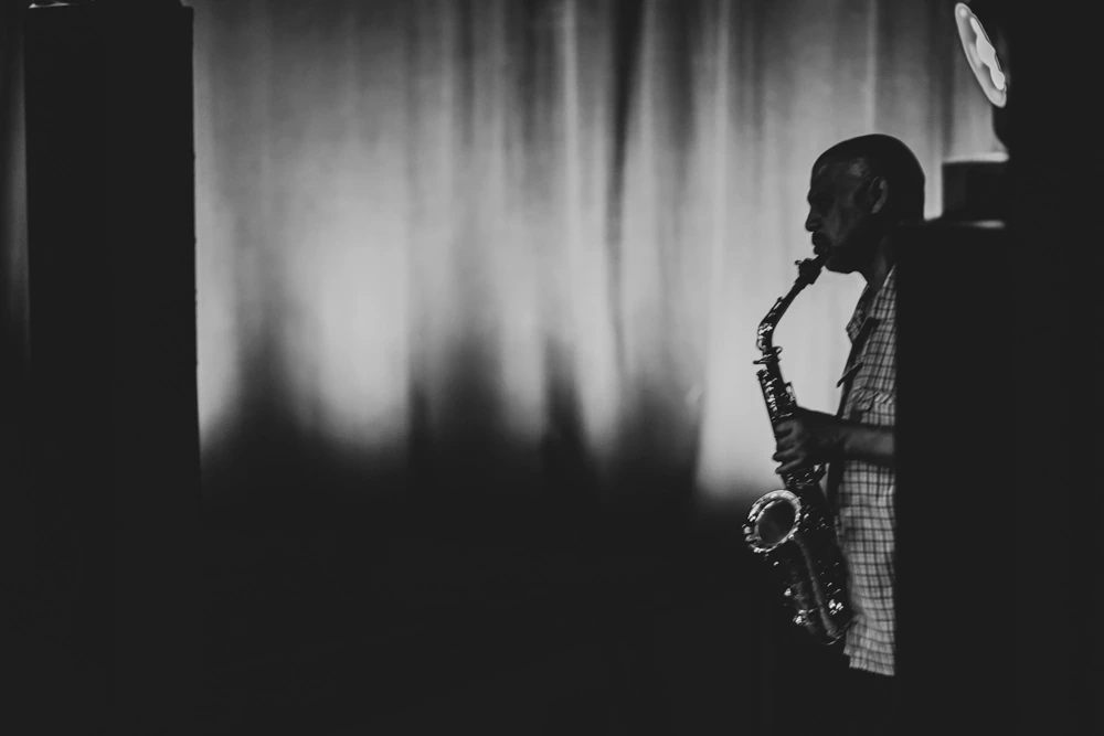 A saxophonist in half-light beside the backdrop.