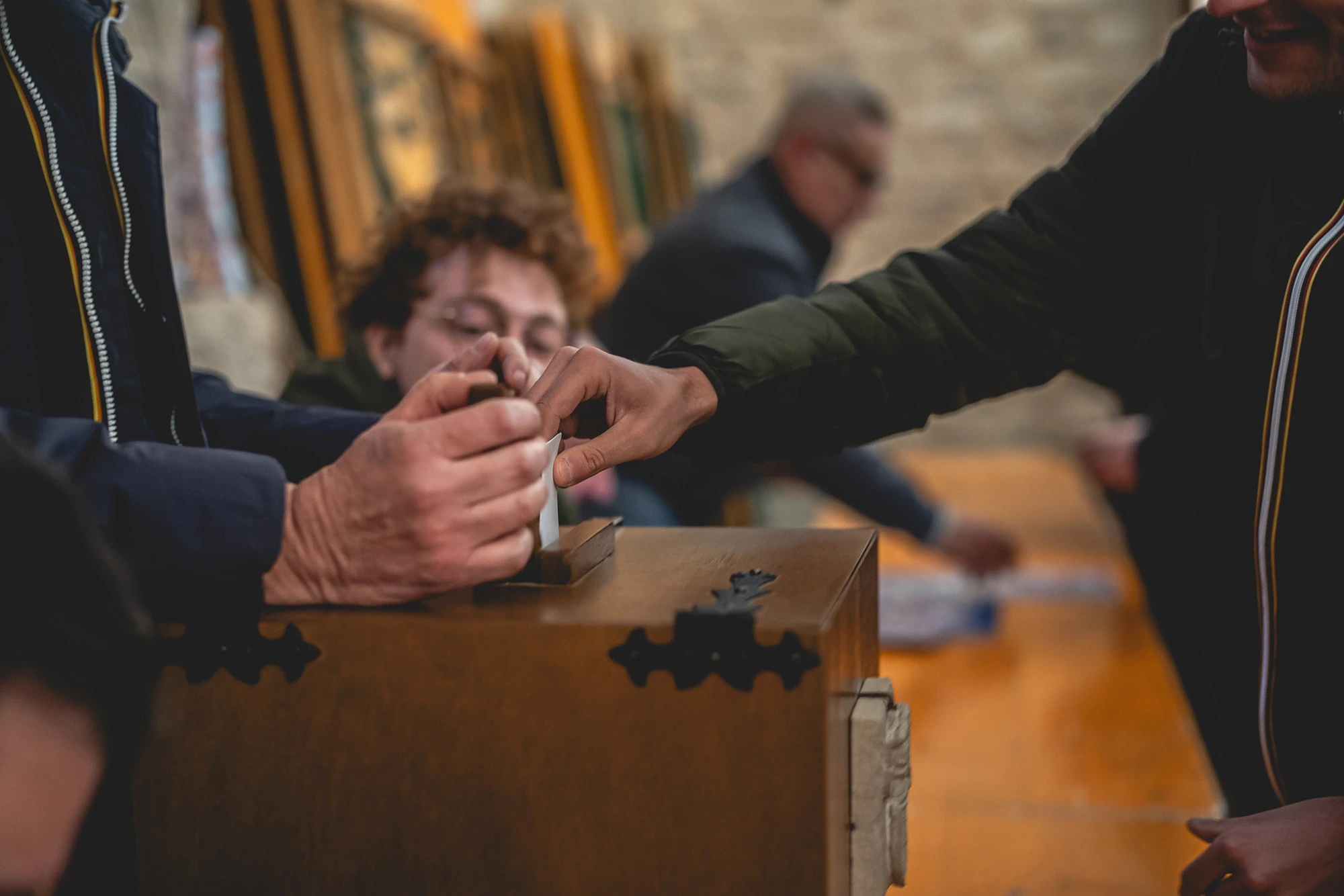 Hands slipping a ballot into a wooden box.