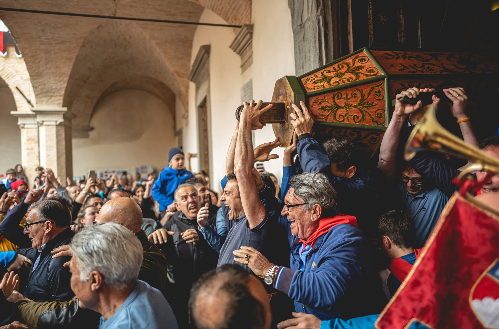 Among raised arms and trumpets, the decorated casket passes over the crowd.