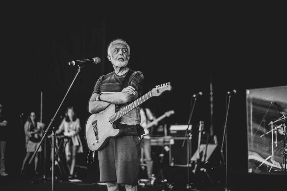 Guitar slung on, arms folded at the microphone, the band behind.