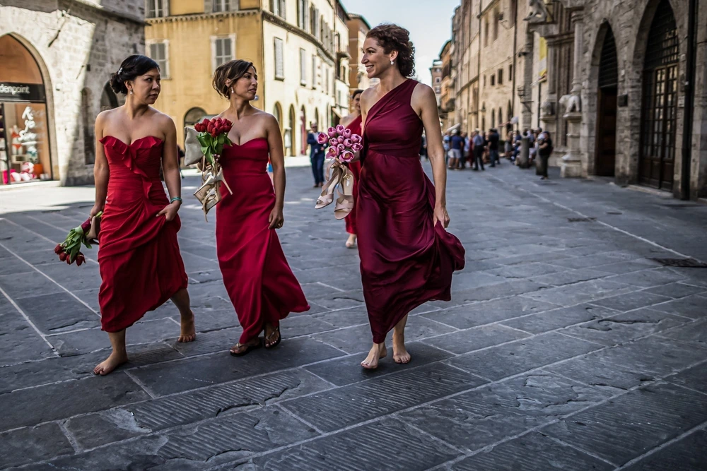 Three women in red walk barefoot over the paving, bouquets in hand.