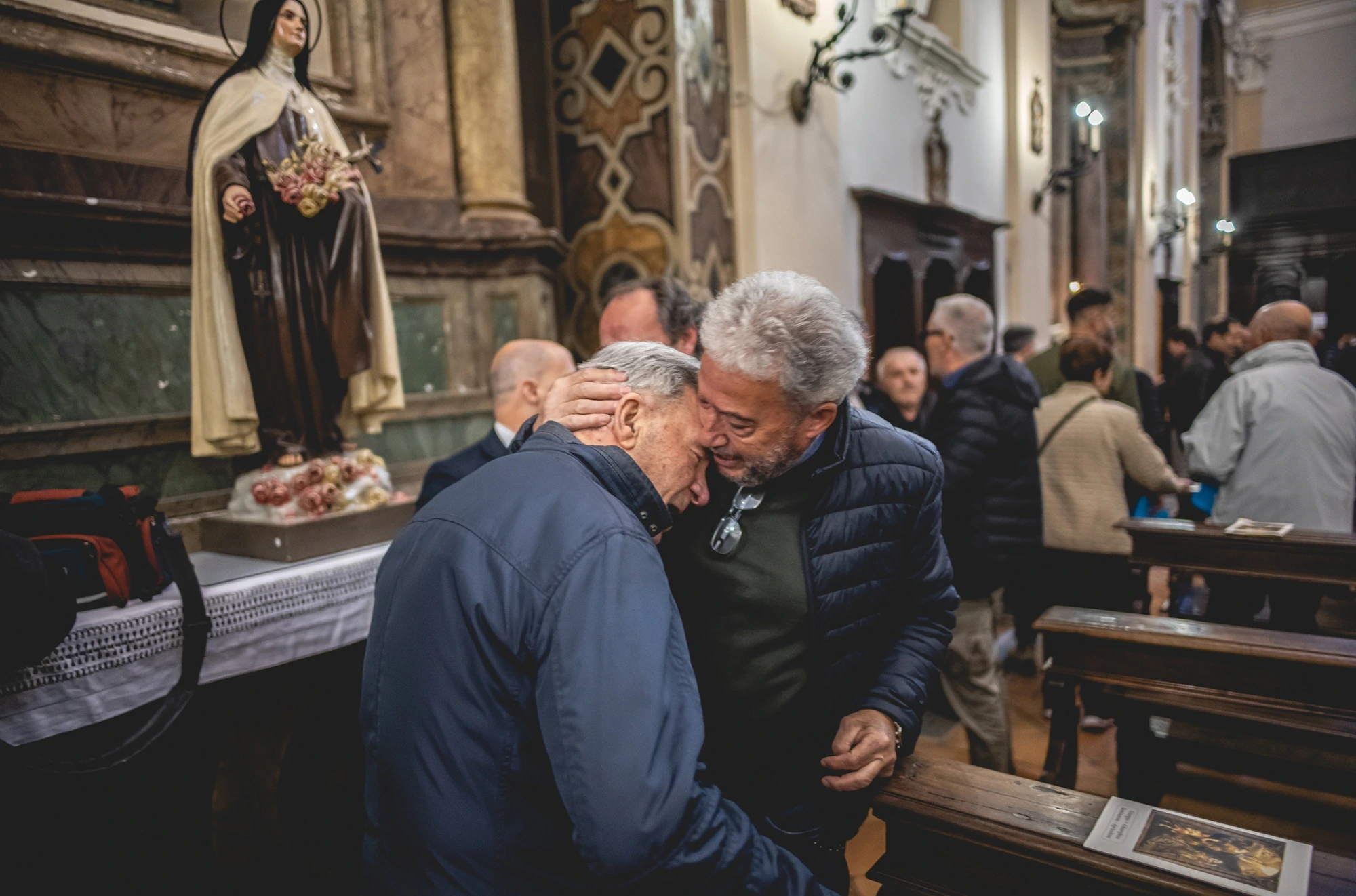 In church, two men embrace beside the statue of the saint.