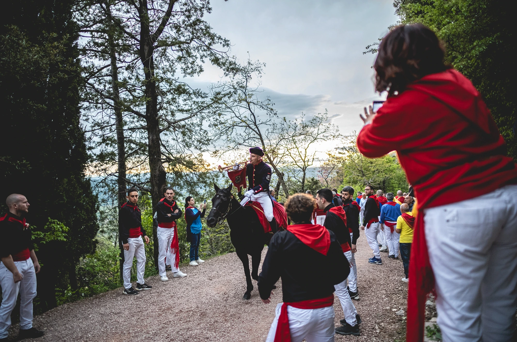 On a path among the trees, a rider and the ceraioli in white and red.