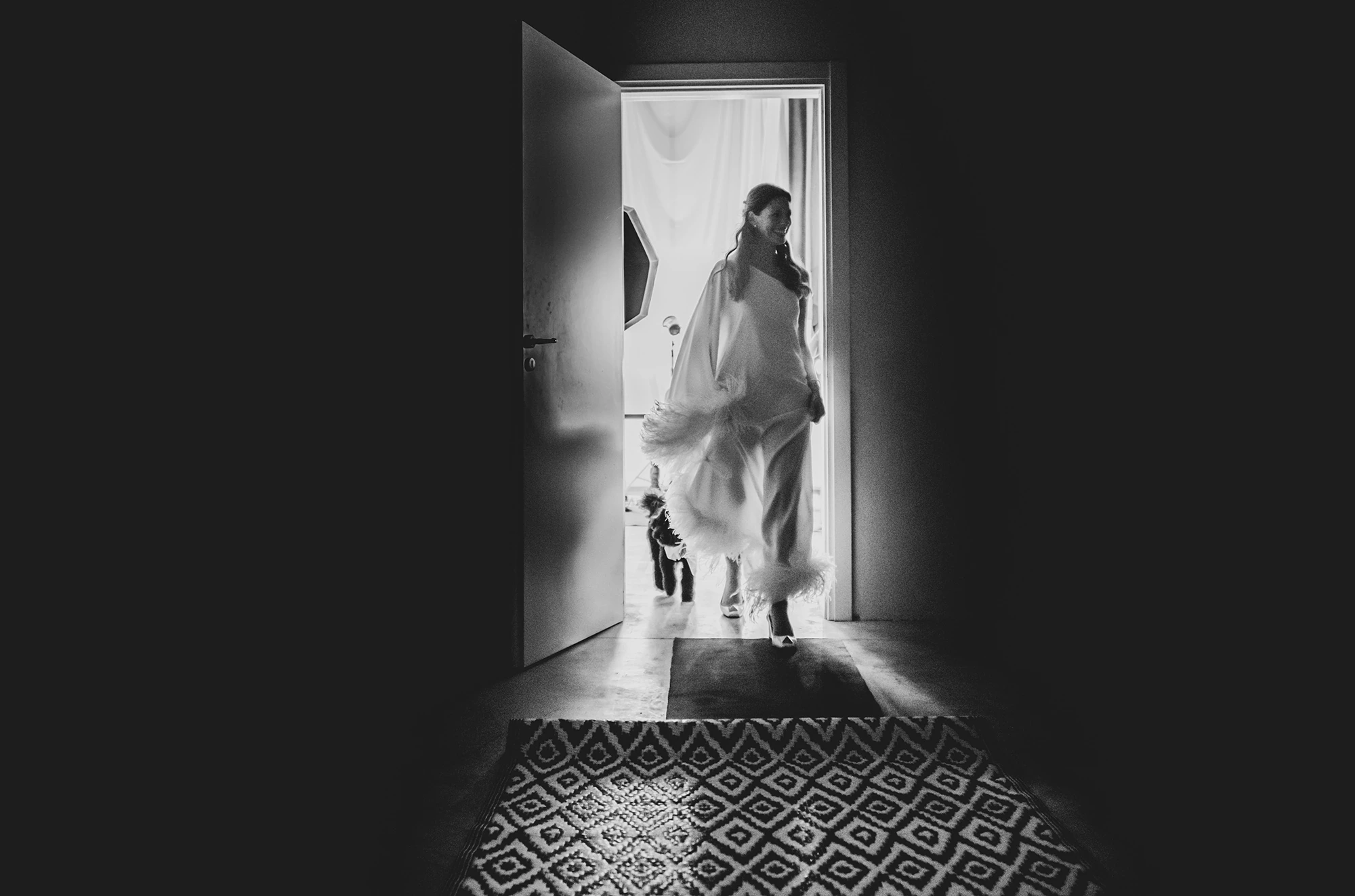 In the lit doorway, the bride steps onto the patterned floor.