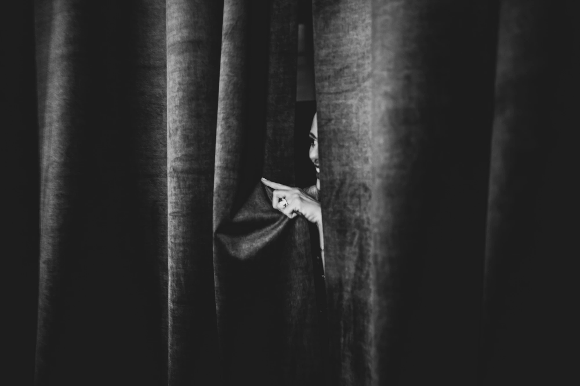 A hand parts the heavy curtain.