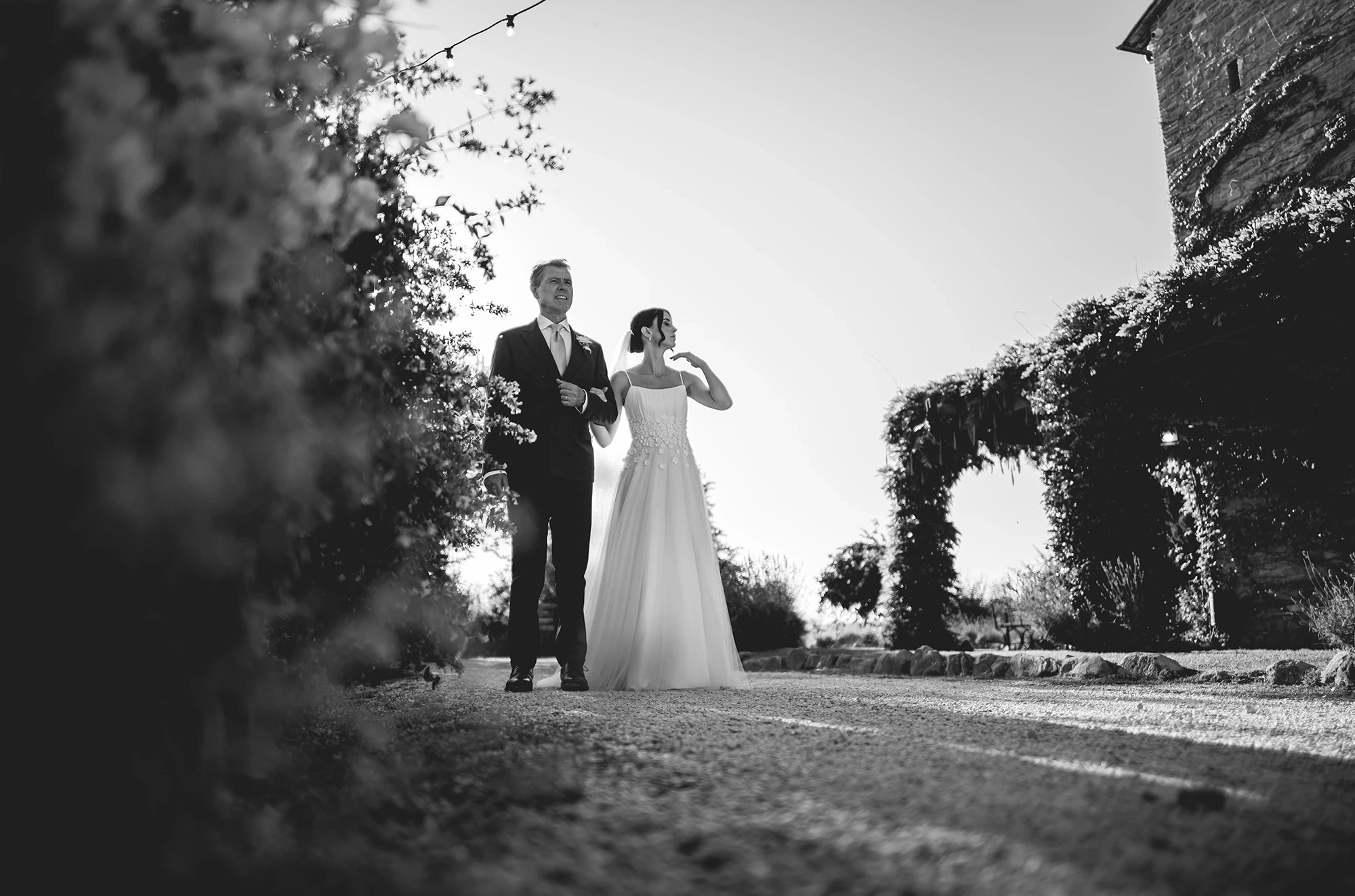 On a path, the couple beside the ivy-covered arch.