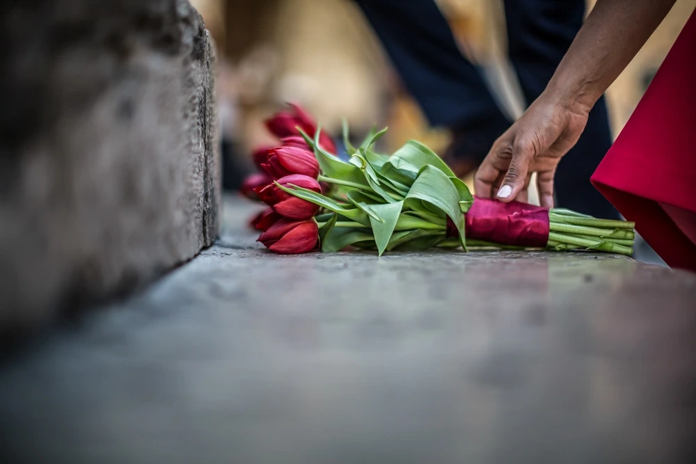 A hand lays red tulips on the stone ledge.