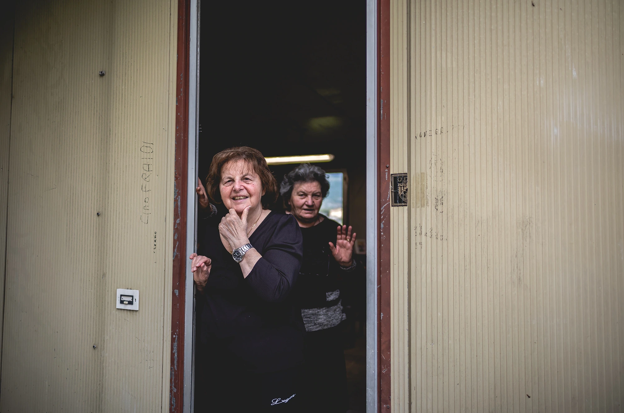 Two women in a doorway; one raises a hand to her mouth.
