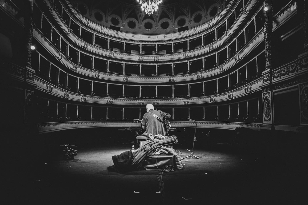In the empty theatre, a lone figure on stage among heaped drapes.