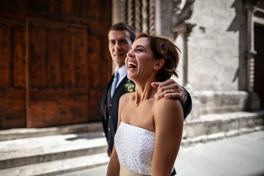 The couple laughing in front of the church's wooden door.