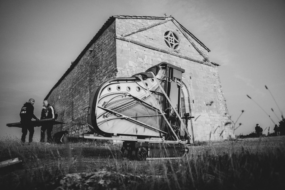 In a field before a stone church, the piano moved on a trolley.