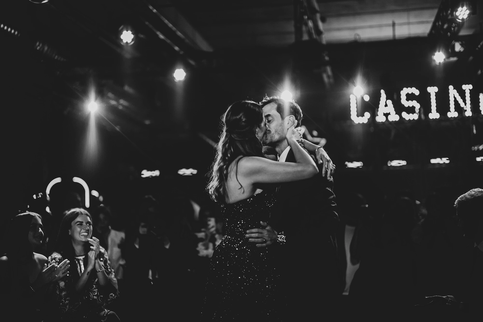 An embrace beneath the illuminated letters, among the crowd.