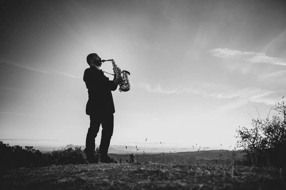 Backlit against the sky, a saxophonist plays in the middle of the field.