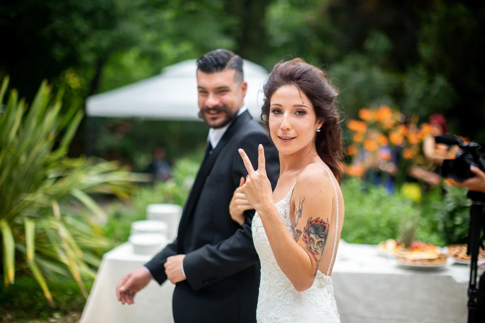 In the garden, the bride makes a victory sign beside the groom.