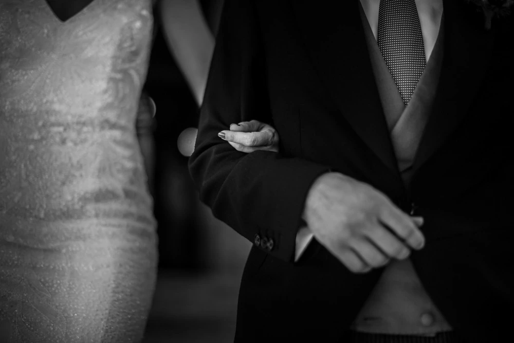 The groom's hand beside the embroidery of the dress.