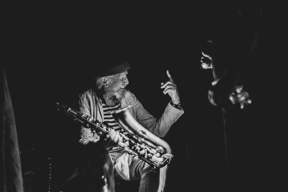 Sax slung on and a finger raised, in a striped shirt and cap.