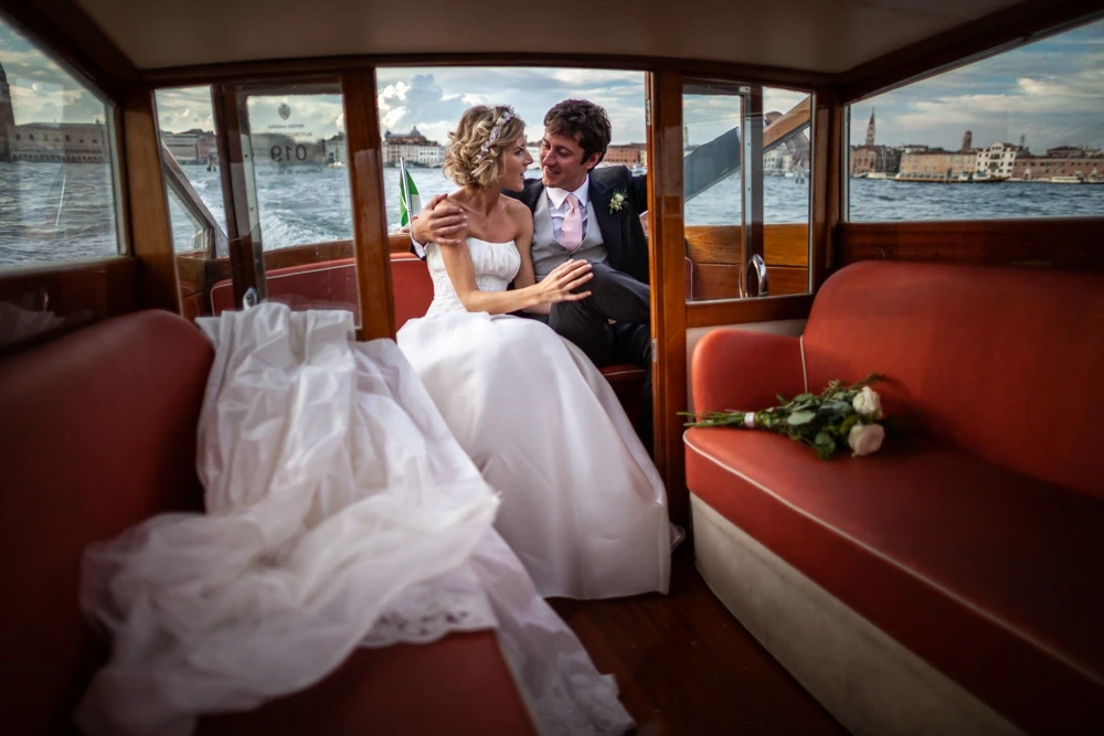 On the red seats of the water taxi, the dress spread out beside the couple.