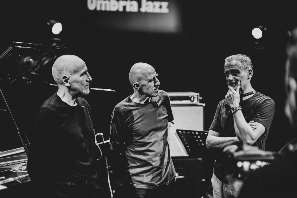 Three men talking on stage, beneath the festival sign.