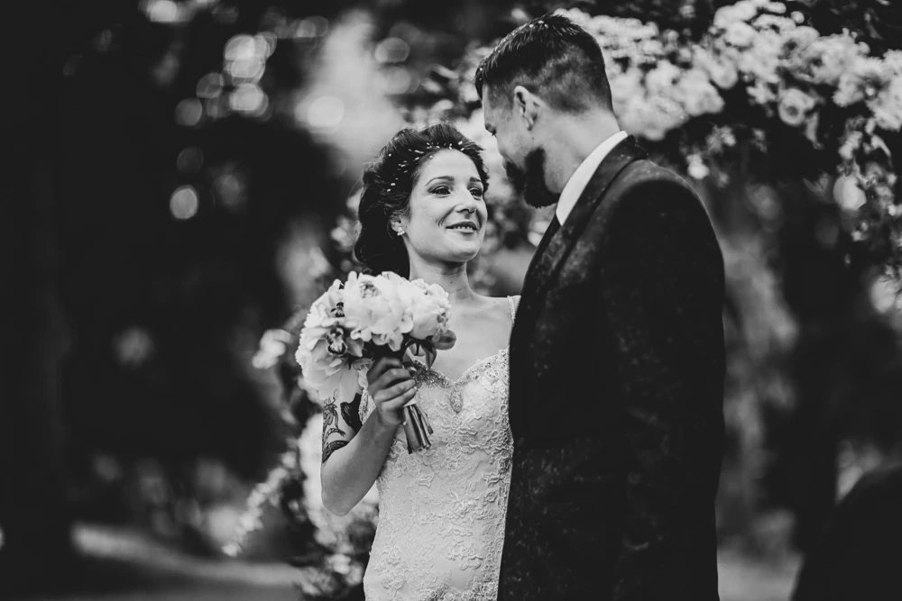 Before the arch of flowers, the bouquet in her hands.