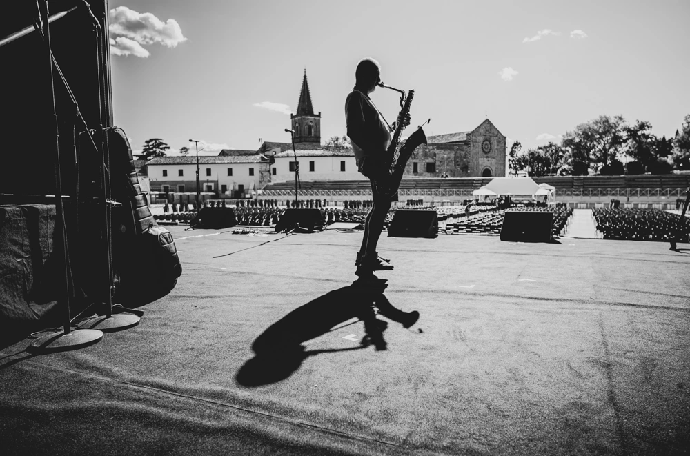 On an open-air stage, a saxophonist alone with his long shadow.