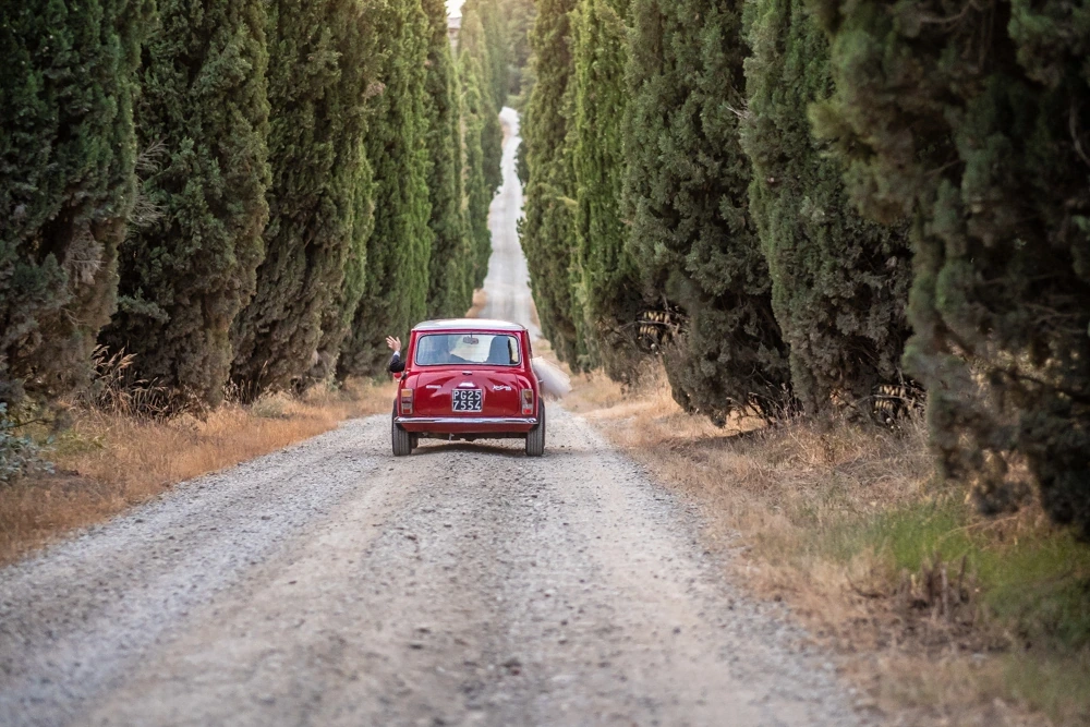 A red Fiat 500 along the gravel road between the cypresses.