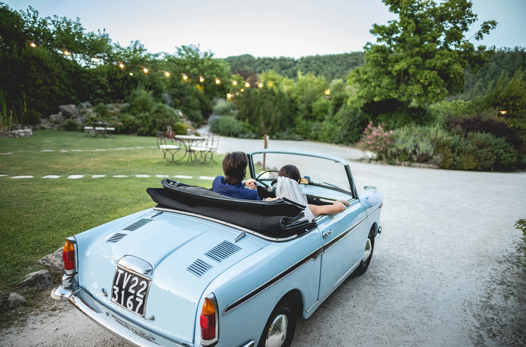 On a lawn, the couple aboard a vintage convertible.