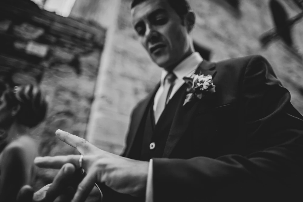 The groom behind an outstretched hand with the ring.