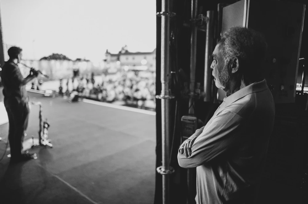At the side of the stage, a man watches with folded arms.