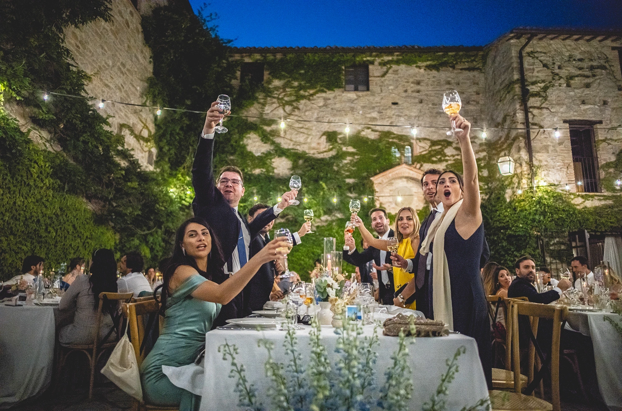 At the outdoor dinner, glasses raised beneath the stone wall.