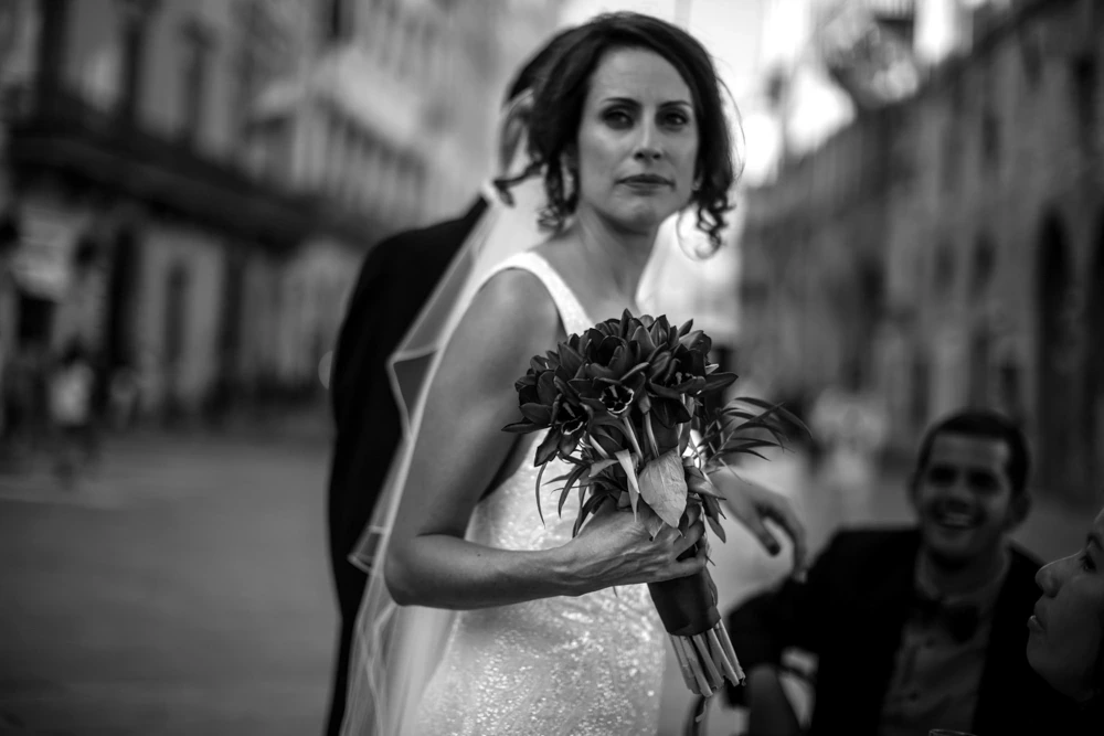 With a dark bouquet, the bride walks along the street.