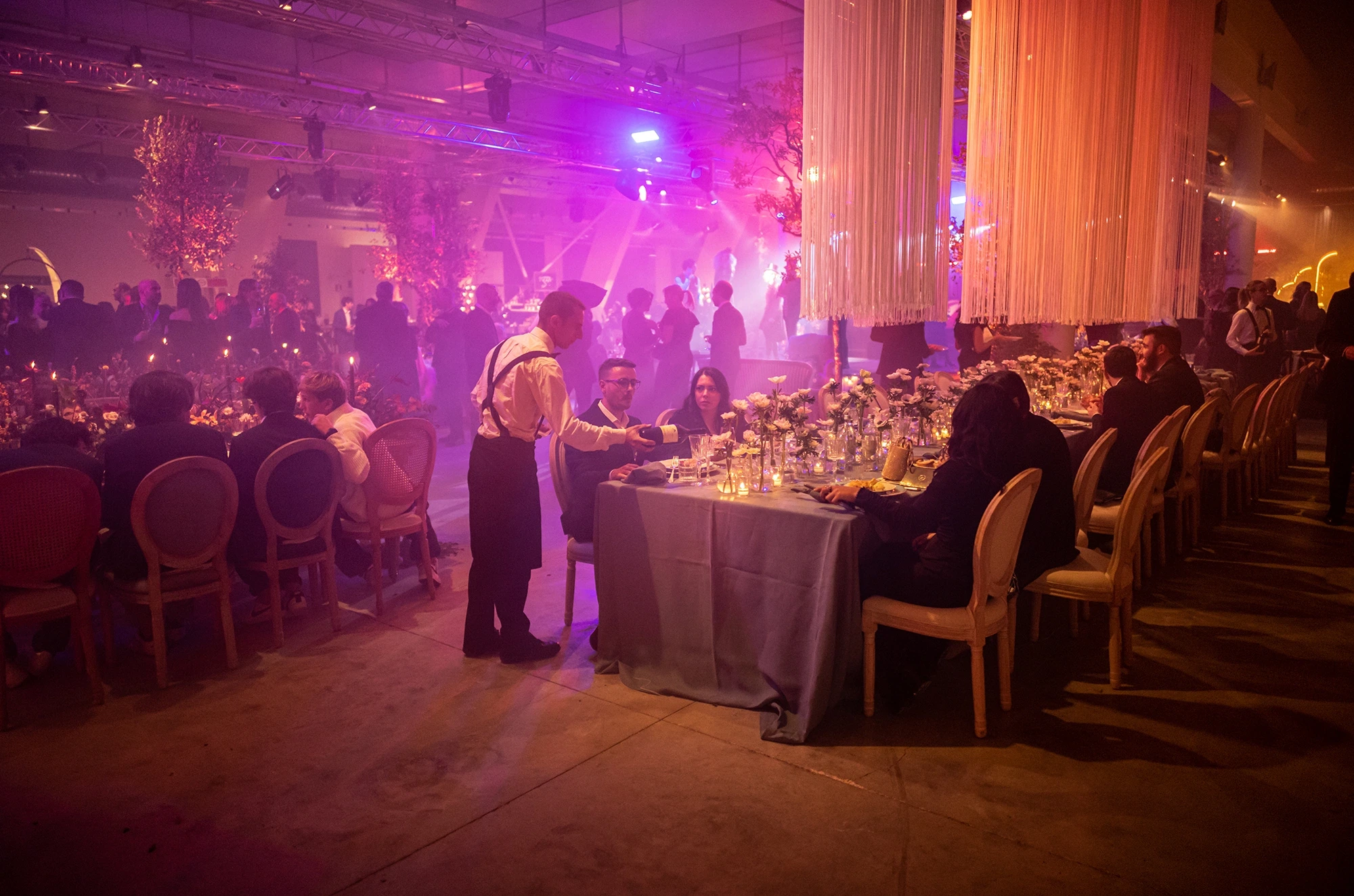 The room in purple and orange light, guests at the tables.