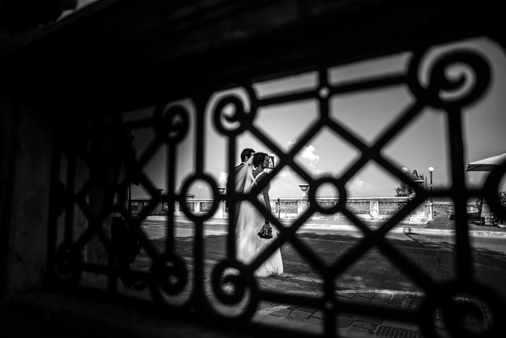 Through the ironwork of a gate, the couple's kiss.