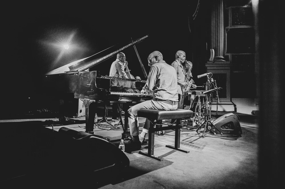 Around the grand piano, the group rehearsing under a beam of light.