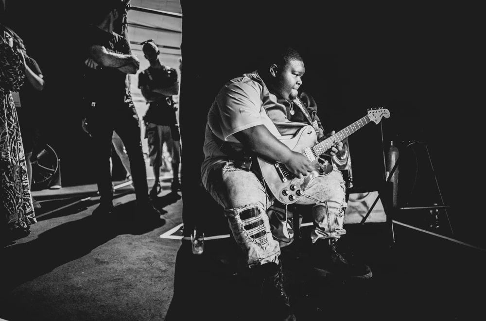 Sitting on the edge of the stage, a guitarist in torn jeans.