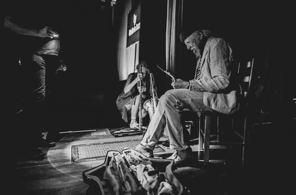 Backstage, a man in a pale suit sits reading.
