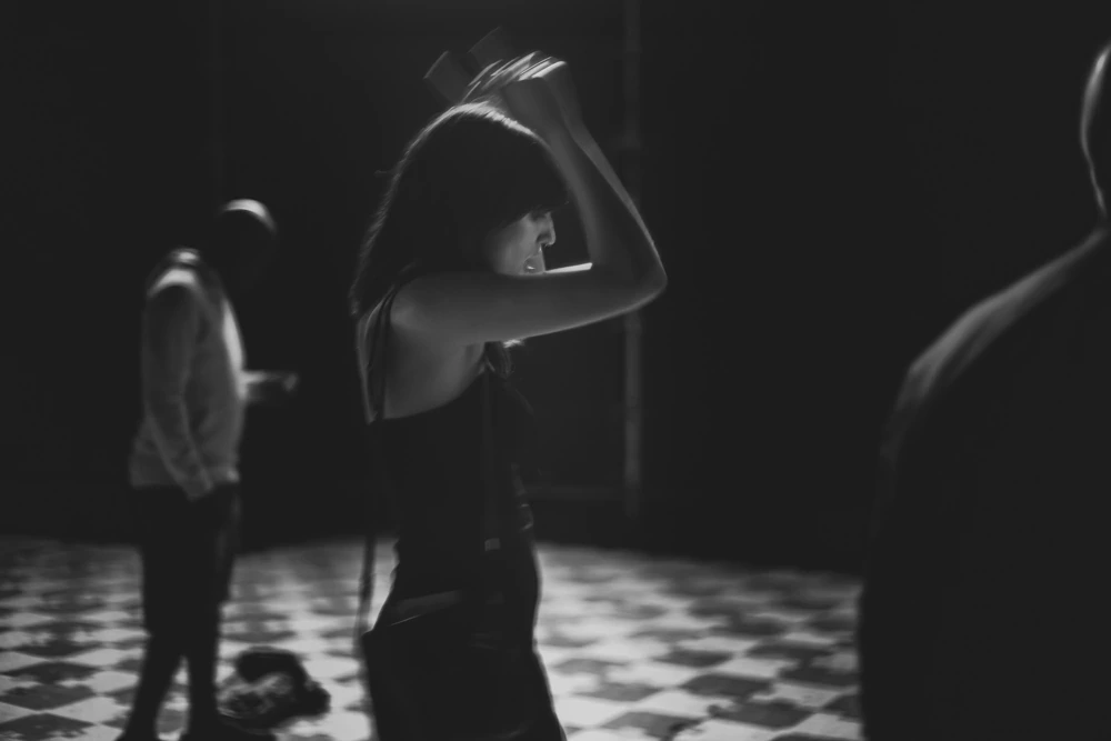 On a chequered floor, arms raised in the half-light.