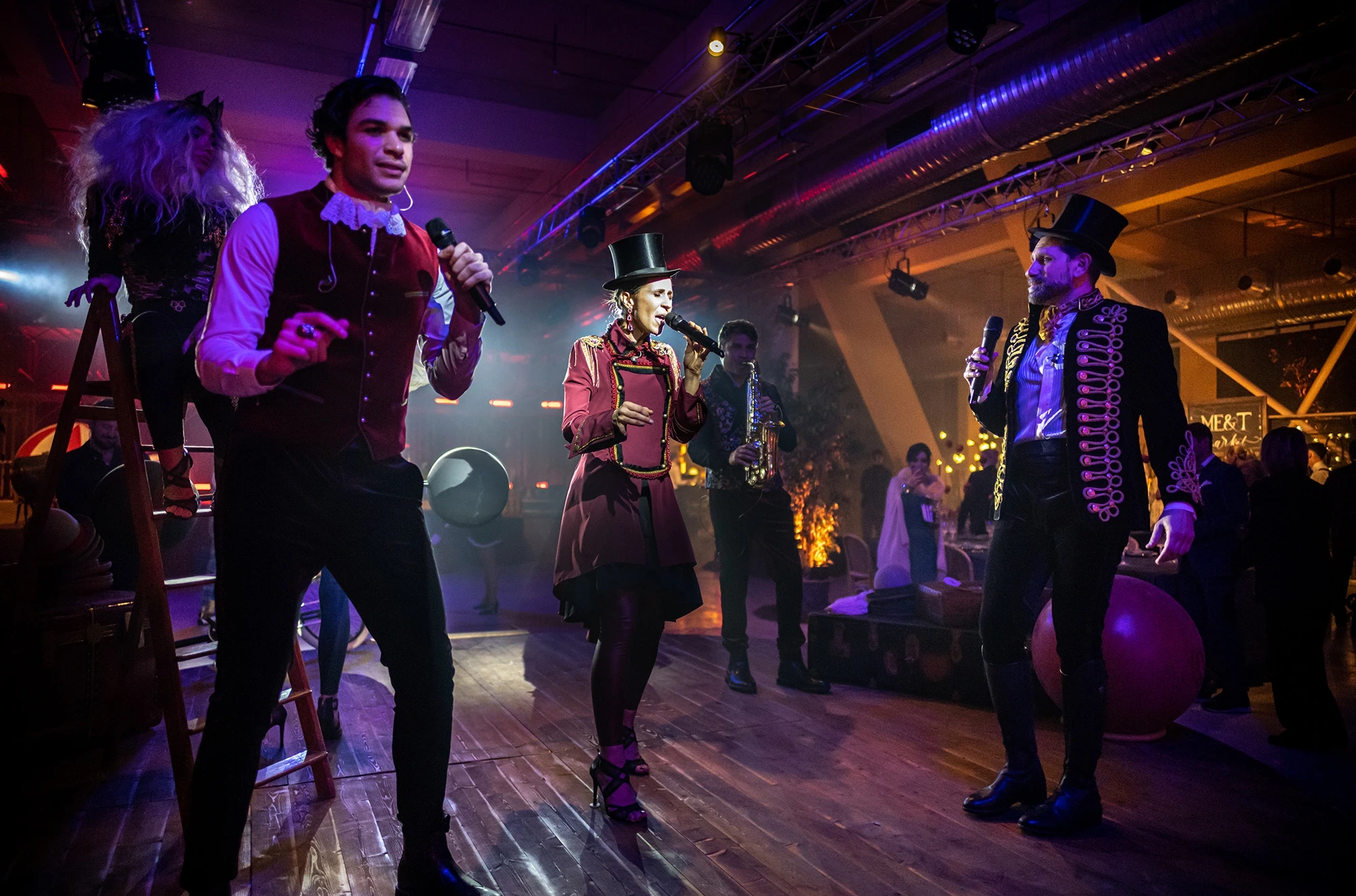Performers in circus costume at the microphone, on the boards.