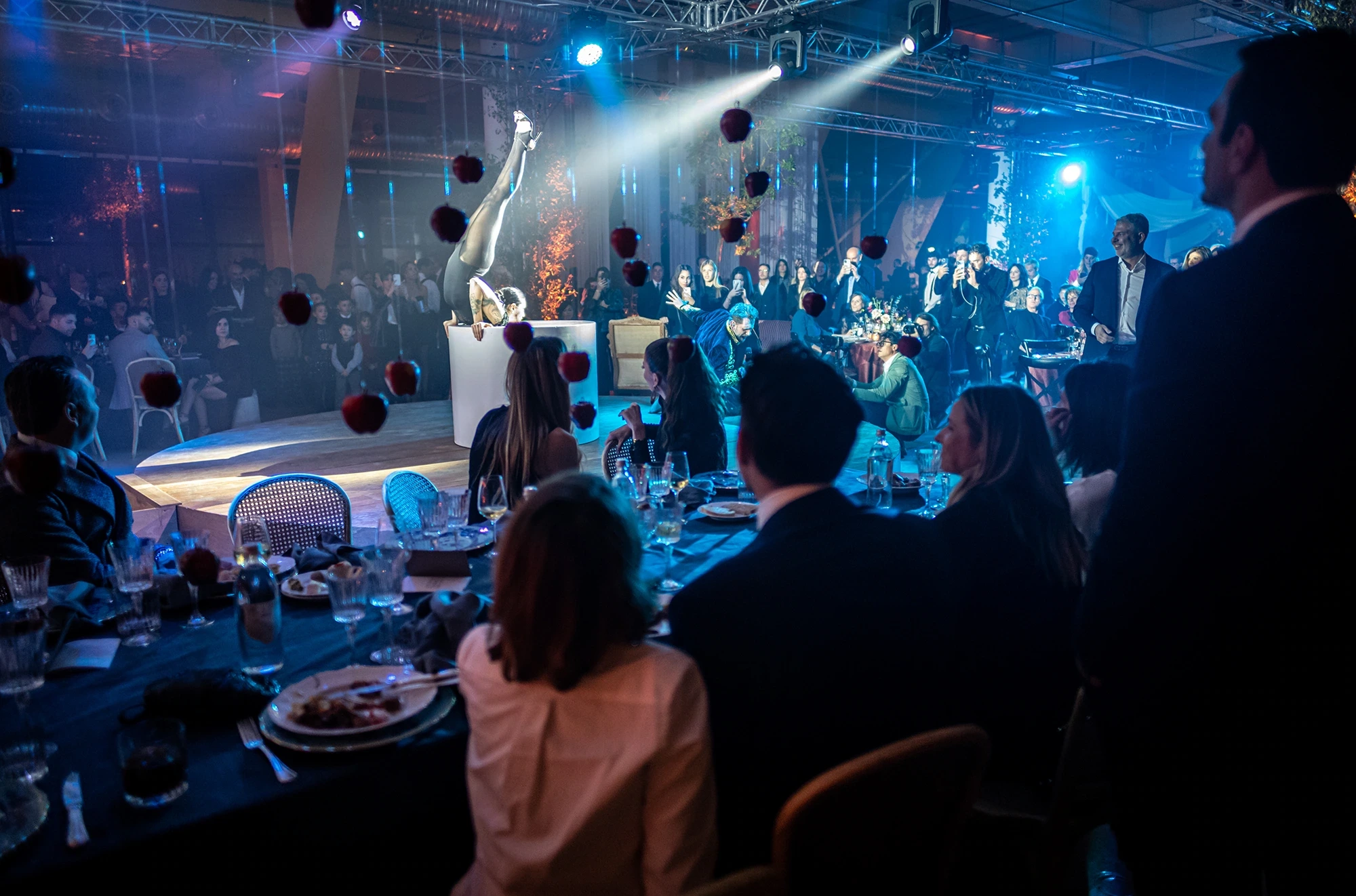 In the big-top hall, guests at the tables and an aerialist above.