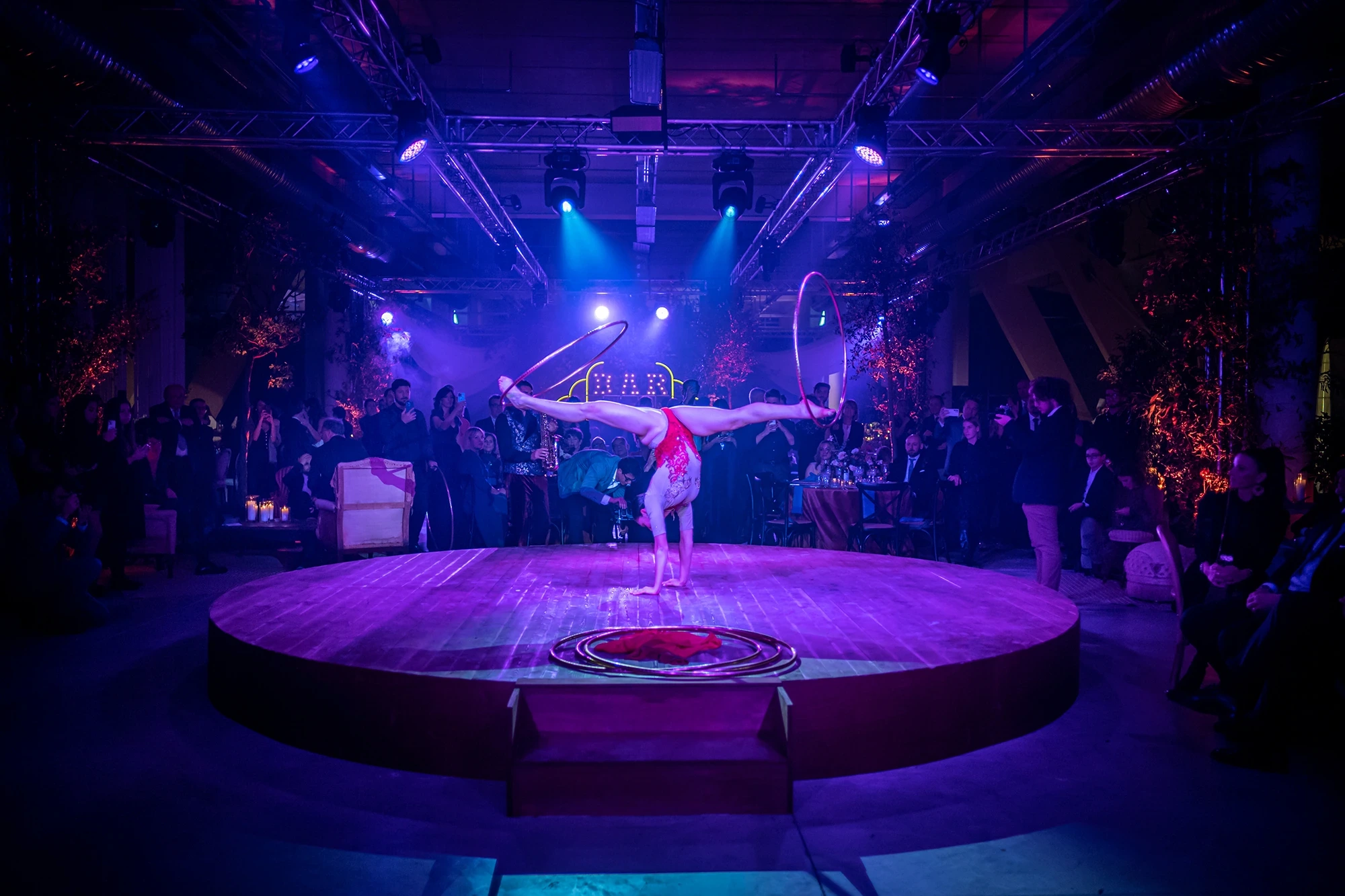 Above the round stage, an aerialist on the hoop in blue light.
