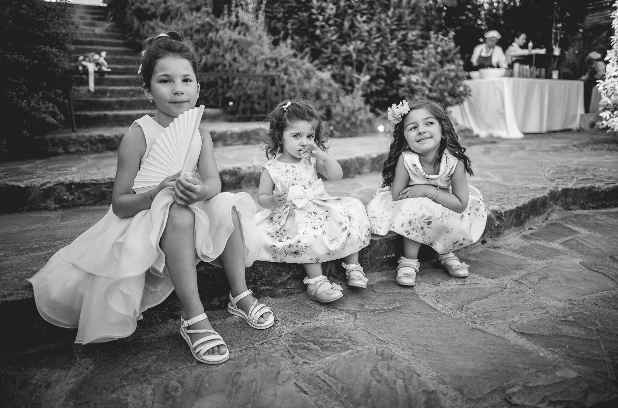Three little girls sitting on the stone steps, one with a fan.