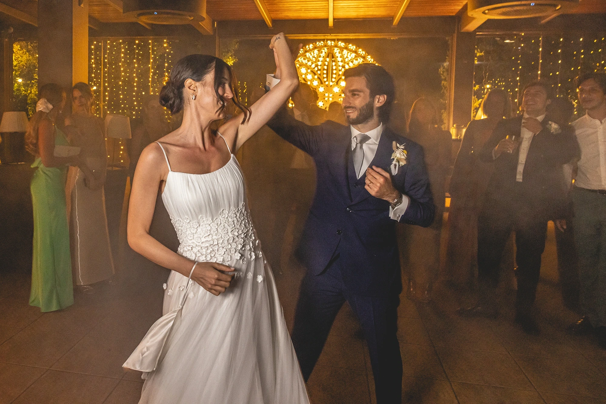 The couple dance hand in hand beneath the chandeliers.