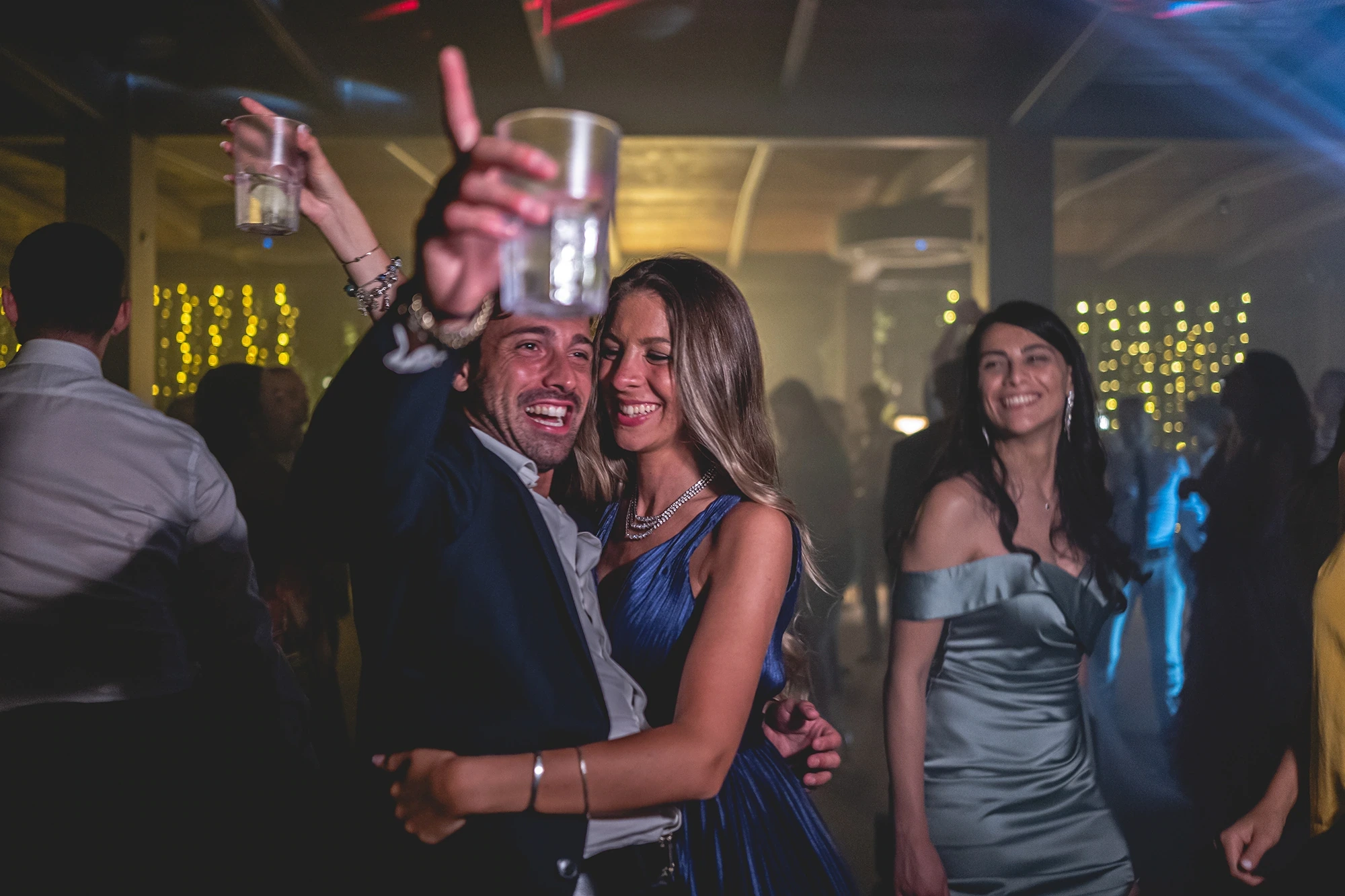 Among the dancing guests, a glass raised high.