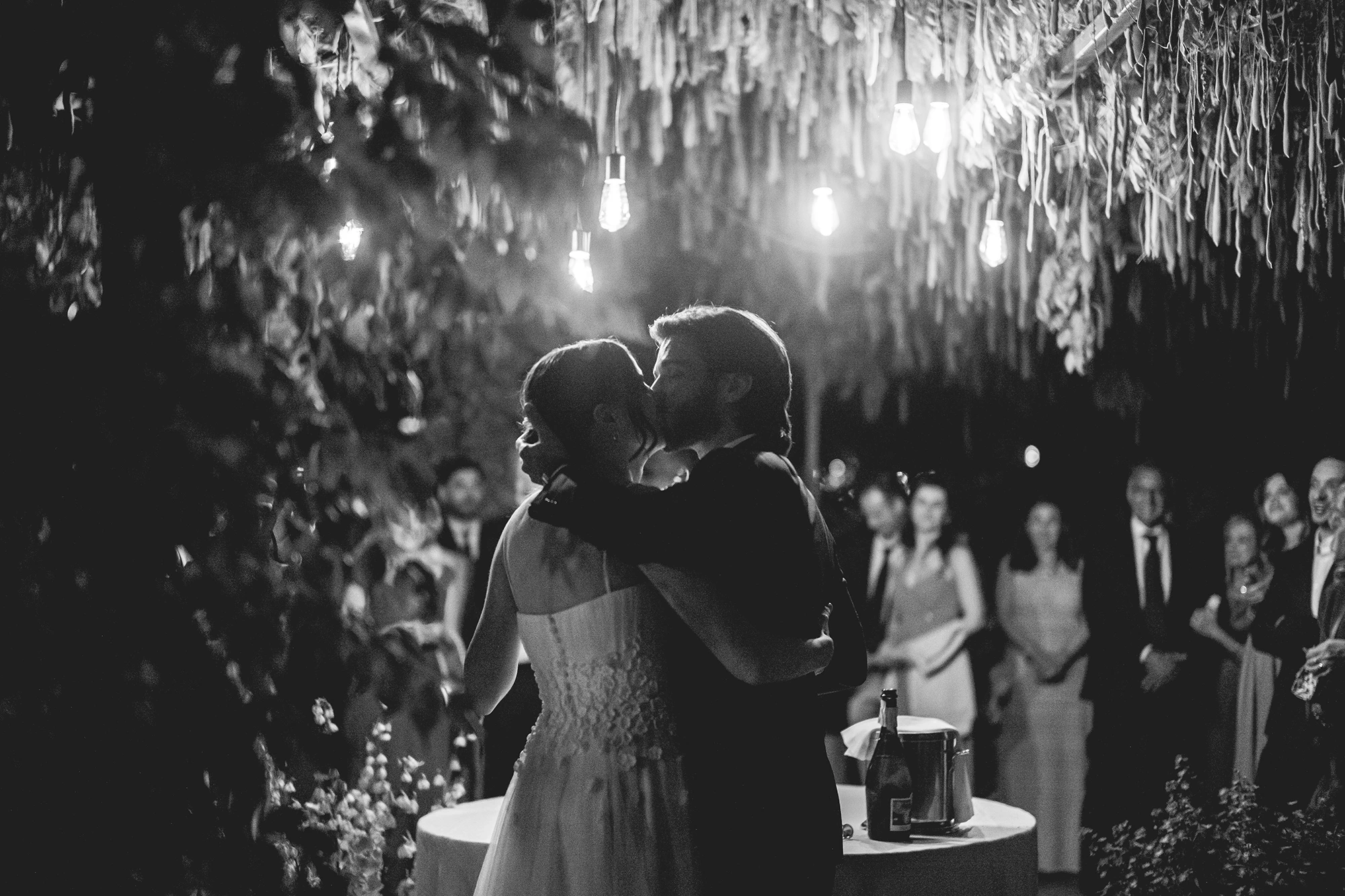 An embrace beneath the hanging lights, before the guests.