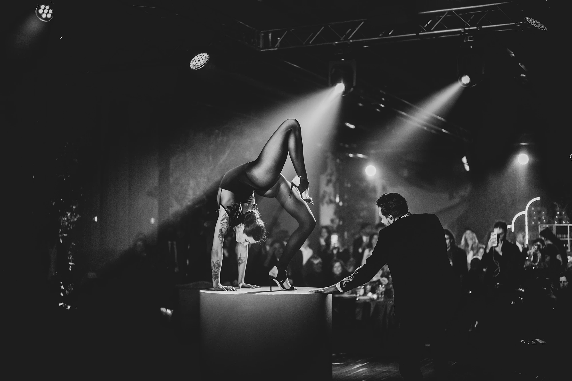 Under the lights, an acrobat in a handstand on a plinth.