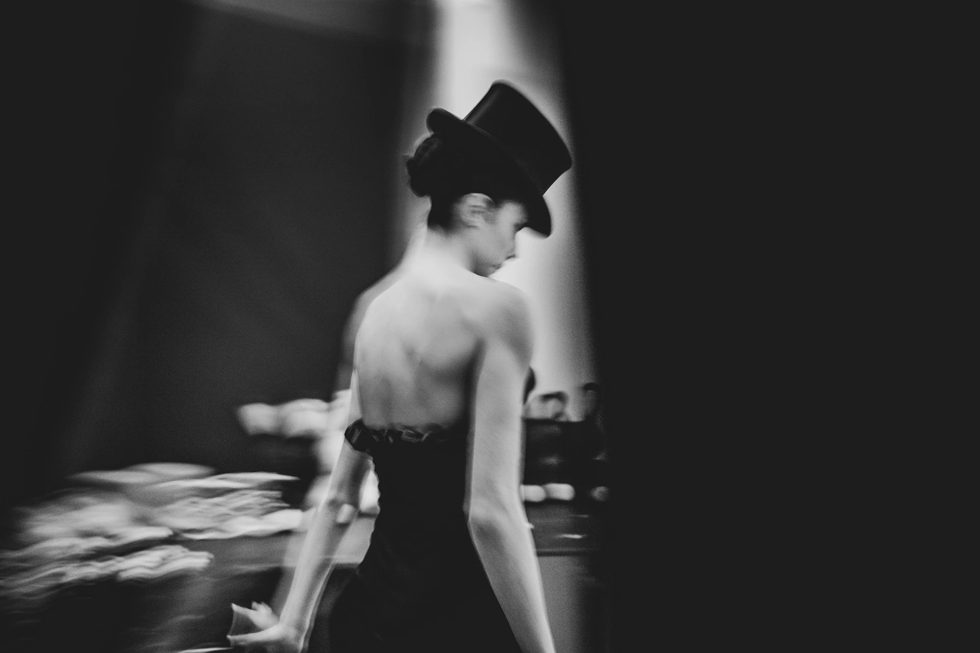 From behind and blurred, a performer in a top hat.
