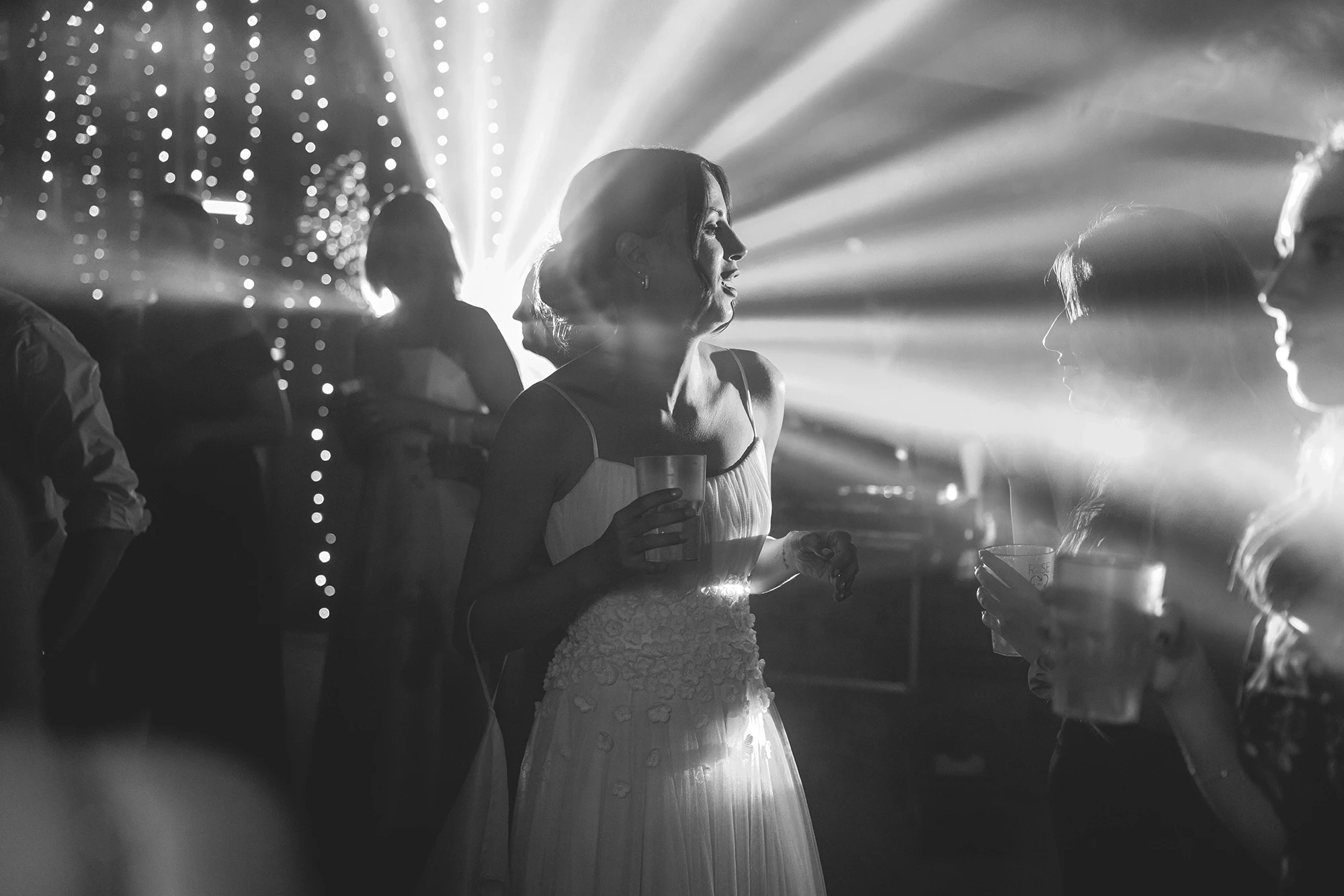 Among the beams of light, a woman with a glass in her hand.